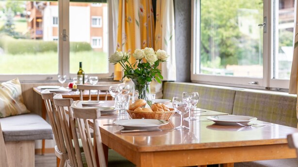 A dining area with a wooden table set for a meal, a vase of white flowers, and a view of greenery and buildings outside. - Group house in Fügen , Zilltertal Arena (Fügen im Zillertal)