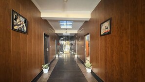 A hotel corridor with wooden walls, potted plants, framed artwork, and a skylight. - KWIK STAY Tapovan (Rishikesh)