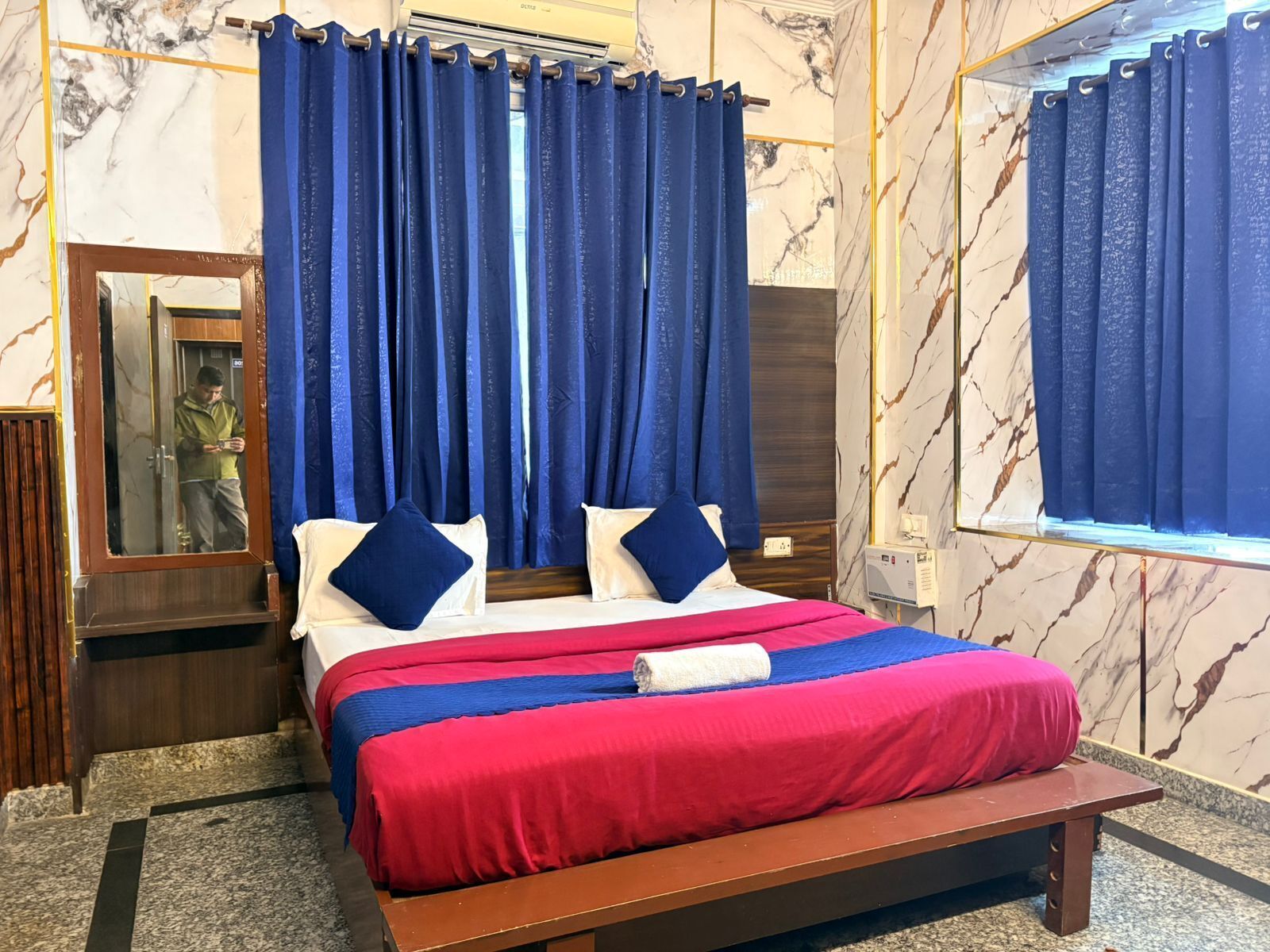 A hotel room with a bed, blue curtains, marble walls, and a wooden bench.