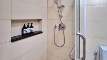 A small, modern bathroom with a glass shower enclosure, a black shelf with toiletries, and a toilet visible to the right.