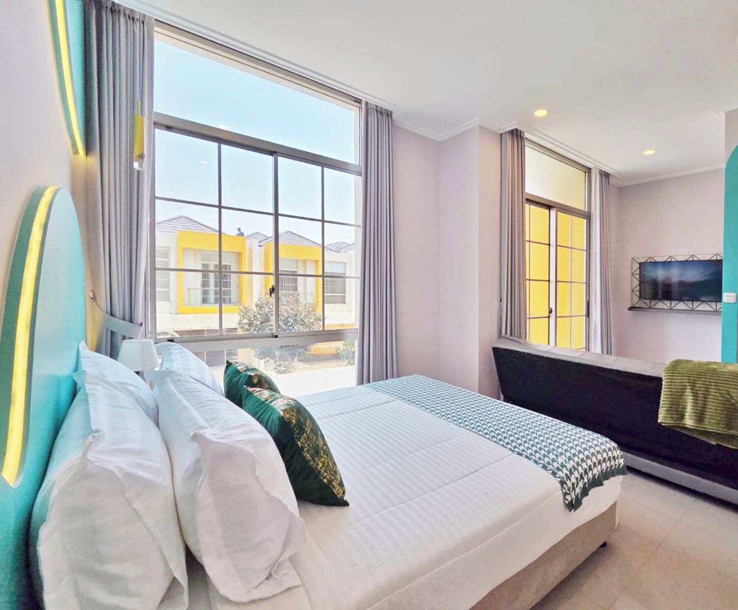 A modern hotel room with a large bed, a TV mounted on the wall, and a view of the outside buildings.