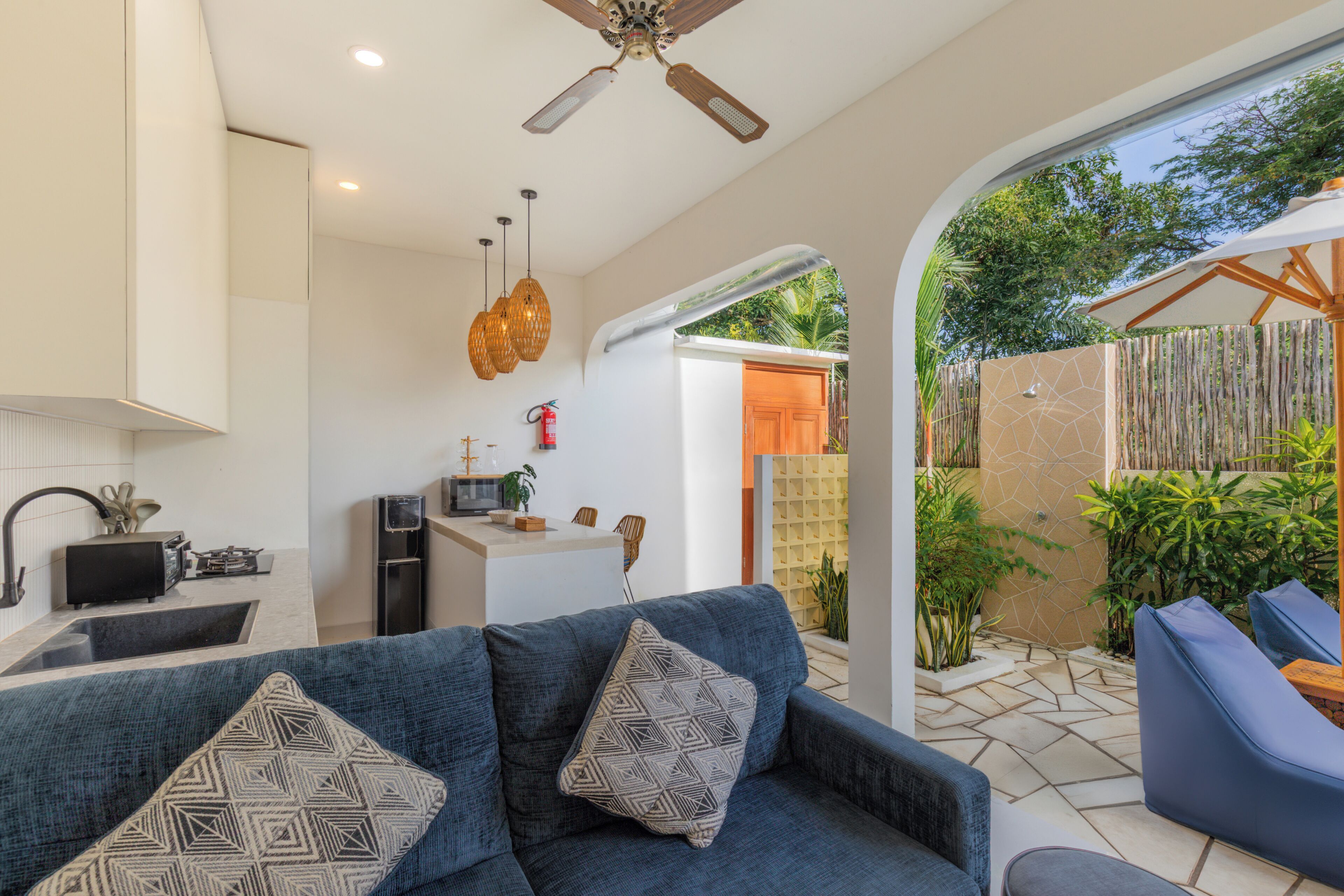 A modern kitchen with a microwave, sink, and stove, a blue sofa with patterned cushions, and a ceiling fan.