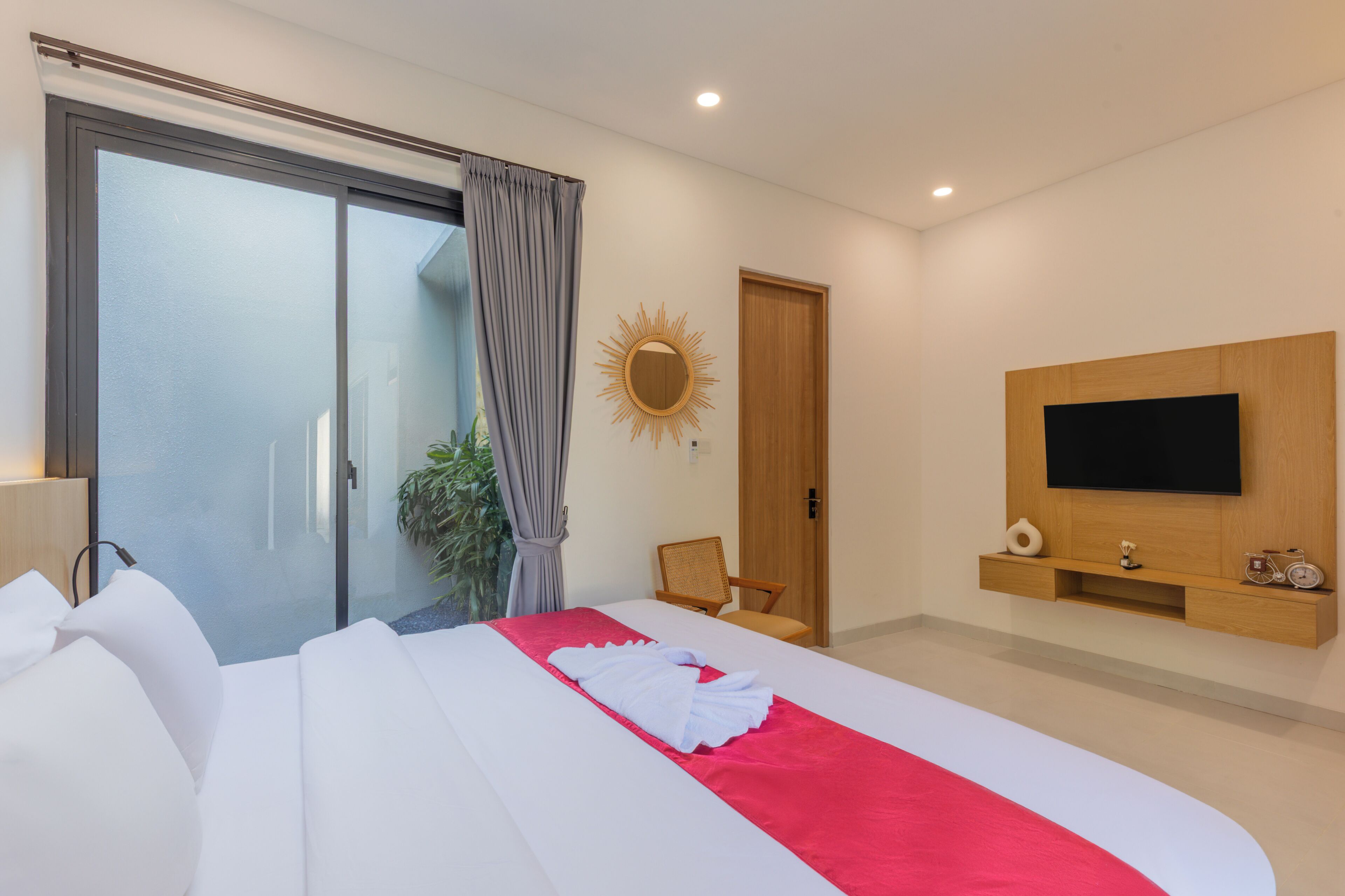 A modern hotel room with a bed, a television, a sliding glass door, a mirror, and a wooden wall panel.