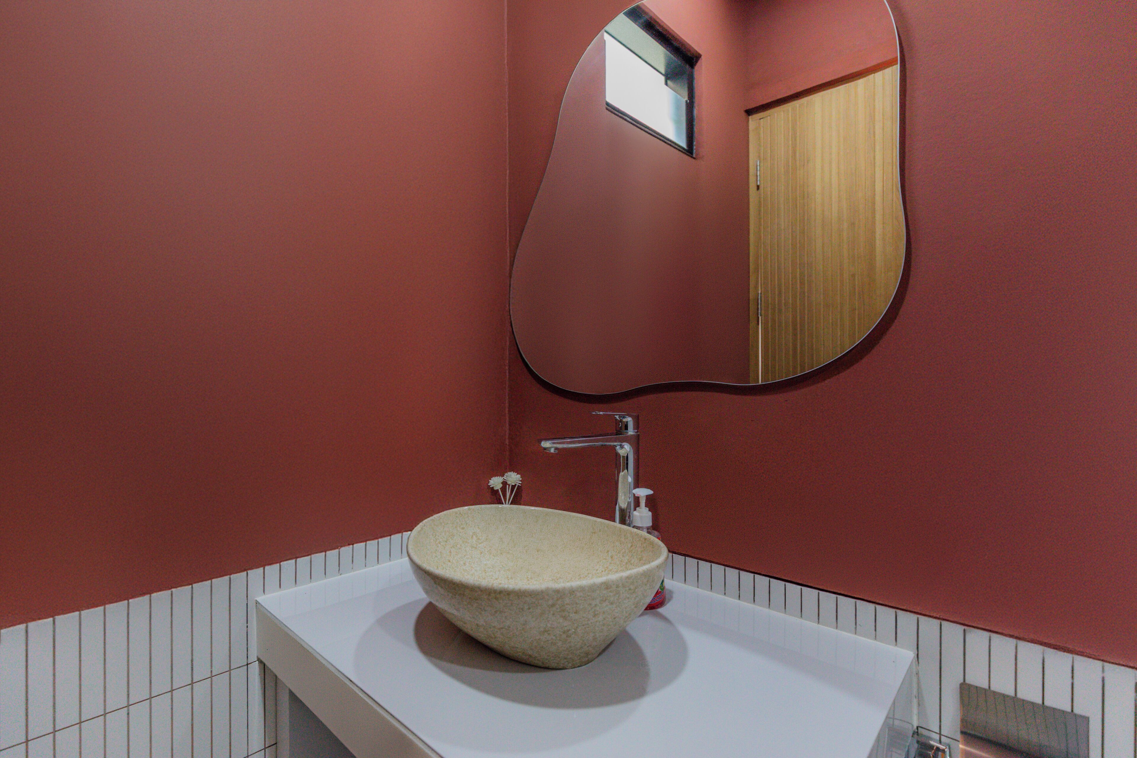 Ein Badezimmer mit einem großen, runden, beigen Waschbecken, einem Spiegel und einer roten Wand.