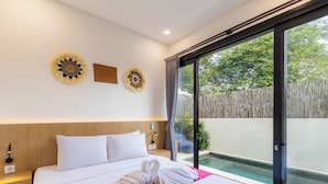 Habitación de hotel con cama, mesita de noche, lámpara de pared y puerta corrediza de vidrio a un espacio exterior.