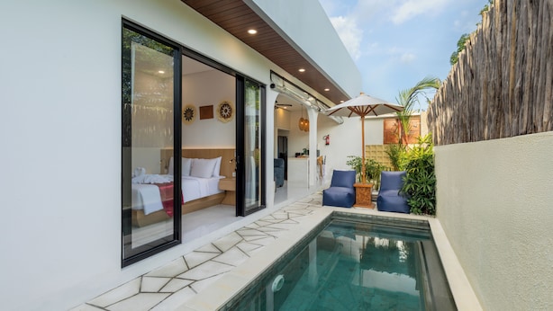 Una habitación de hotel moderna con puerta de cristal, piscina y zona de patio con sillas y plantas.
