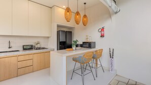 Una cocina moderna con armarios de madera, una isla central con taburetes altos, un microondas y un extintor en la pared.