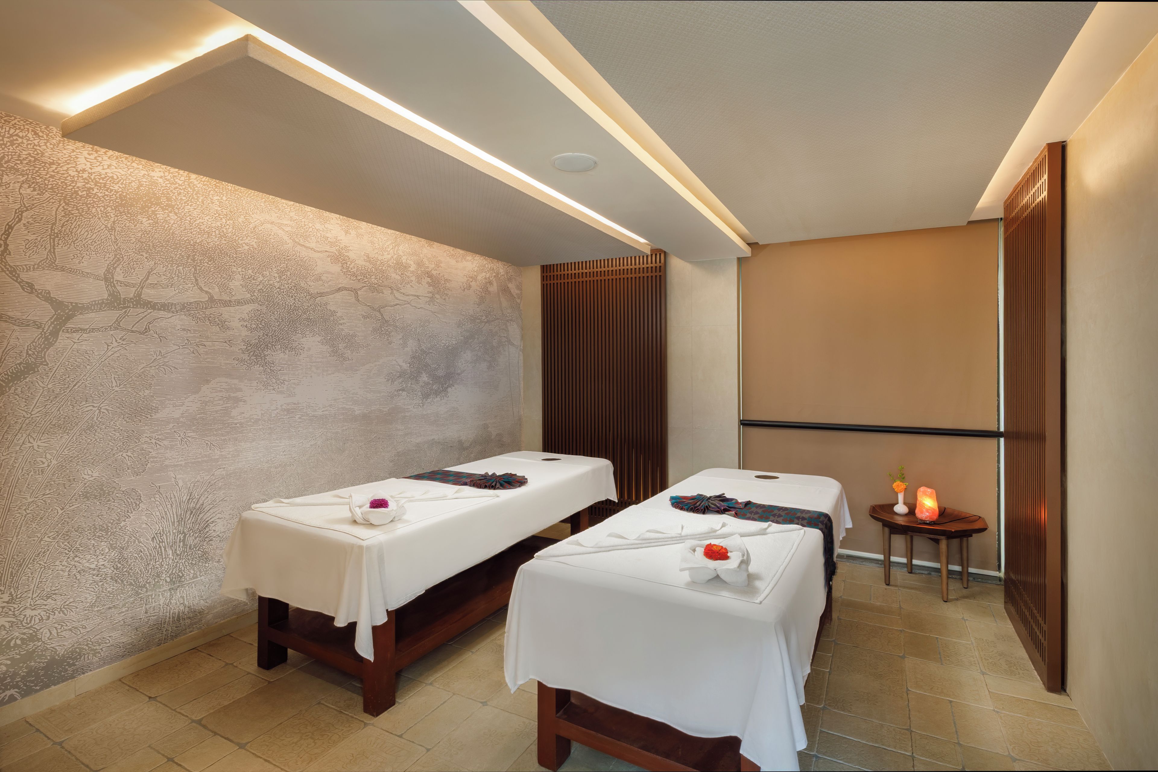 Un cuarto de spa con dos camillas de masaje, un revestimiento de pared de madera y una mesita con piedras calientes.