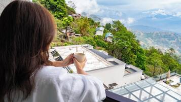 A person holding a cup, overlooking a mountainous landscape with houses.