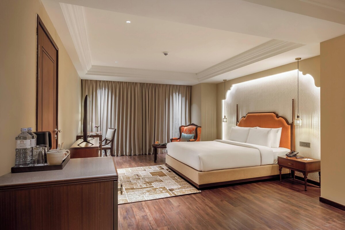 Une chambre d’hôtel avec un grand lit, un bureau agrémenté d’un plateau de produits de toilette, une chaise, une table de chevet et une vue sur l’extérieur à travers les rideaux.