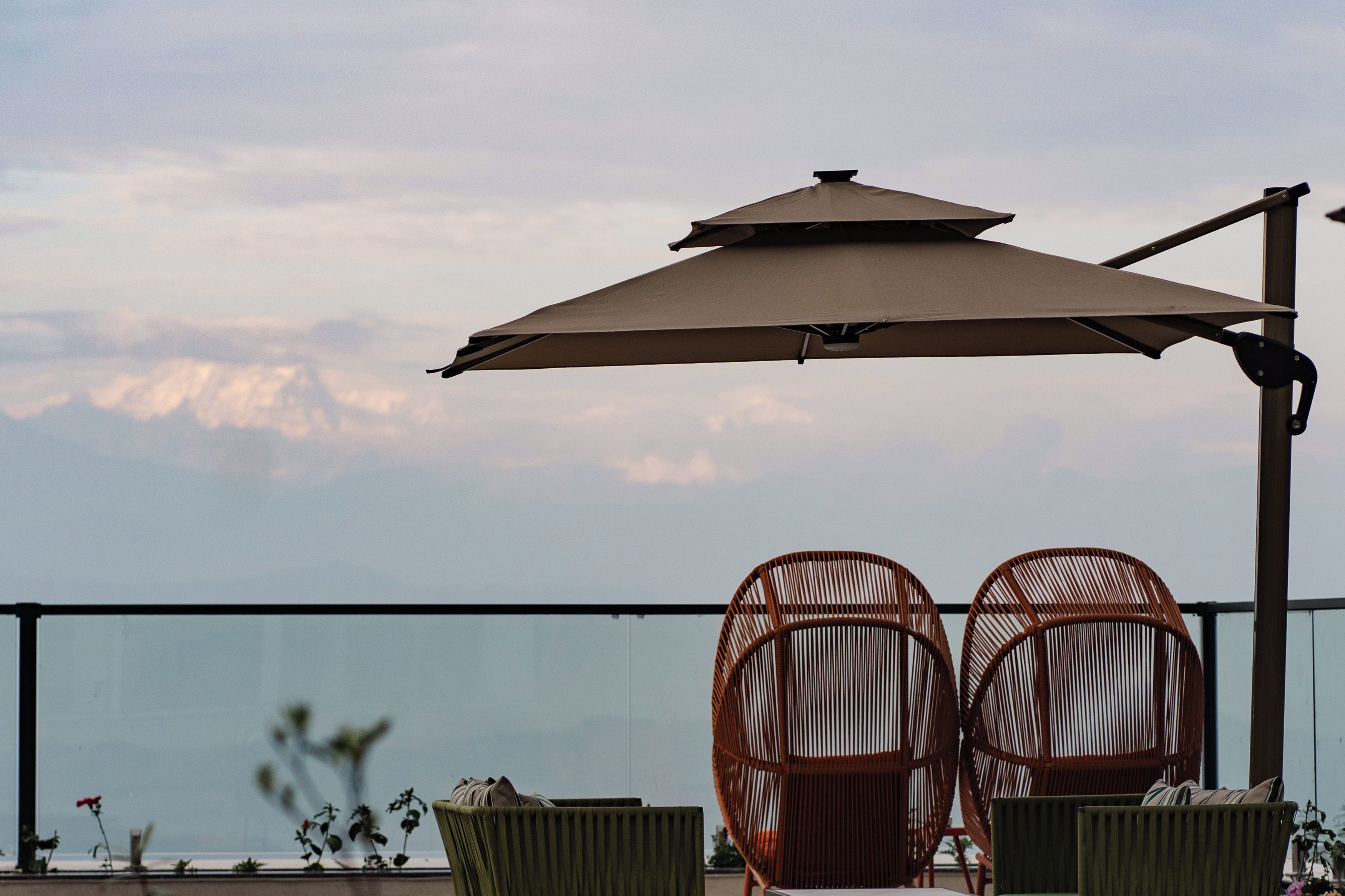 Two wicker chairs with cushions, a large umbrella, and a view of a mountain range.