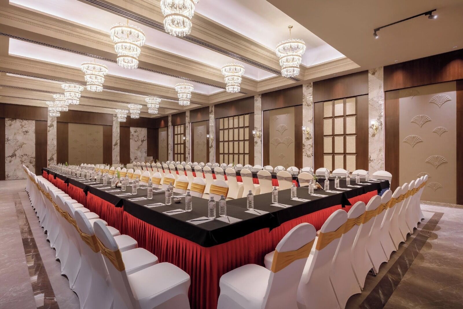 A conference room with a long table, white chairs with gold sashes, and chandeliers.