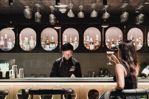 Eine Bar mit mehreren hängenden Lampen, ein Mixologe bereitet ein Getränk zu.