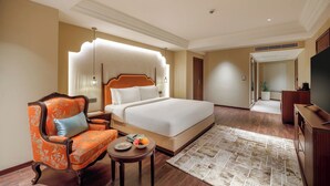 Hotelkamer met een groot bed, een stoel, een klein tafeltje met een fruitschaal en een televisie.