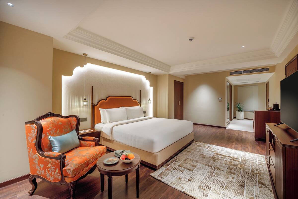 Una habitación de hotel con una cama grande, una silla, una mesita con un cuenco de fruta y un televisor.