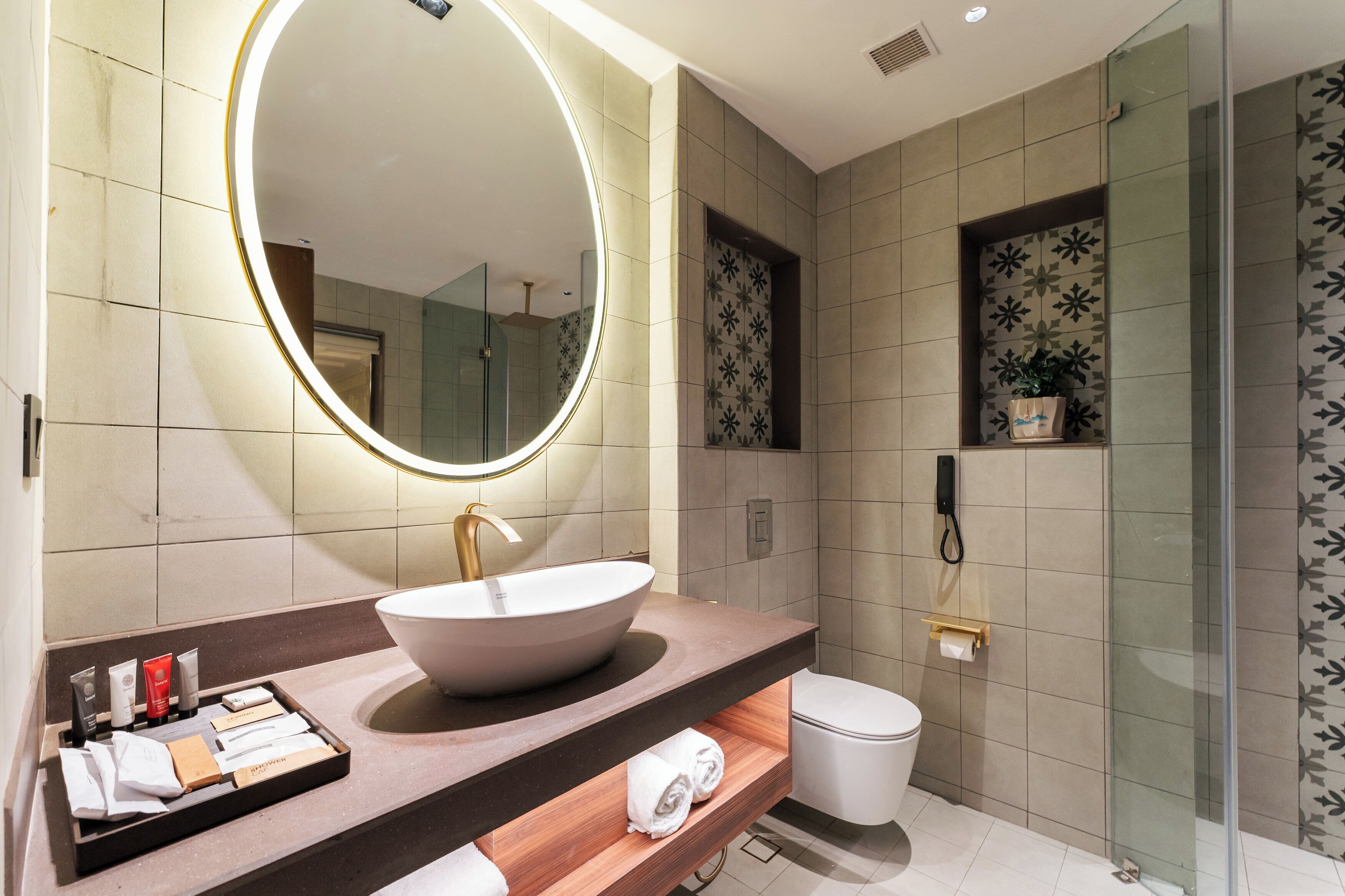 Un baño moderno con un espejo ovalado grande, un lavamanos sobre encimera, un inodoro y una zona de ducha.