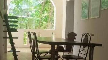 Un coin repas avec une table et des chaises, une fenêtre en arc de cercle donnant sur un paysage verdoyant et un ventilateur de plafond.