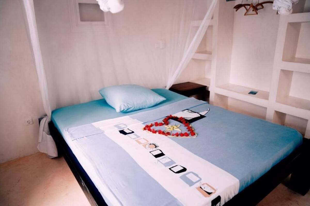 A bed with a blue bedspread, a white canopy, and a small bedside table with a lamp.