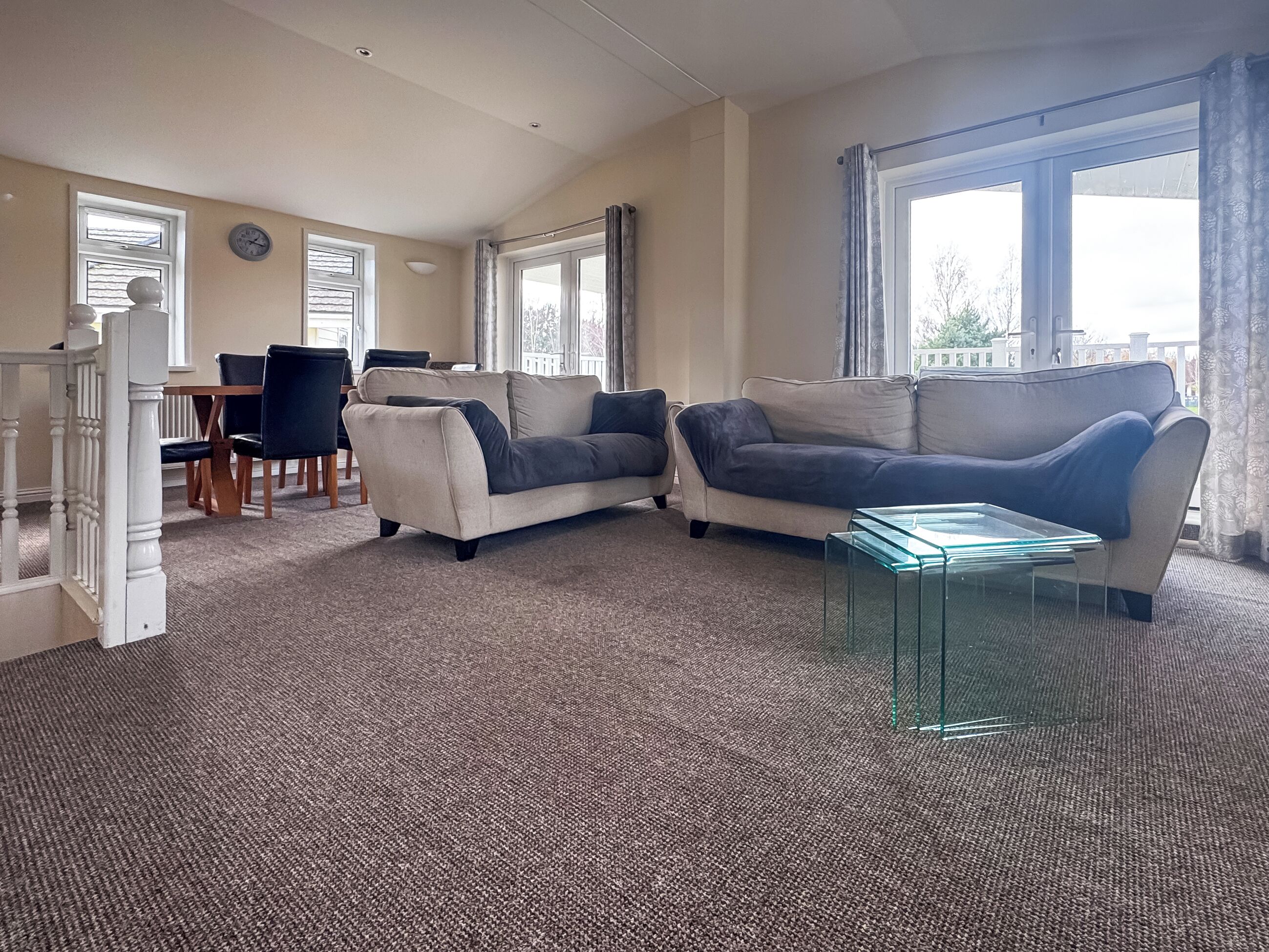 A living room with a beige sofa, a glass coffee table, and a dining area with a table and chairs.
