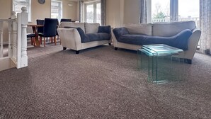 Una sala de estar con un sofá color beige, una mesa de centro de vidrio y un comedor con mesa y sillas.