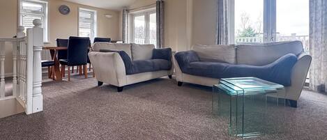 A living room with a beige sofa, a glass coffee table, and a dining area with a table and chairs.