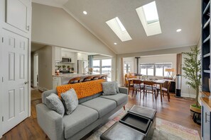A spacious living area with a gray sofa, a coffee table, and a dining area with a table and chairs. - Hike, Fish & Golf: Waterfront Gem on Camp Lake! (Sparta)