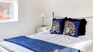 A bed with a metal frame, white bedding, and two decorative pillows with peacock designs.