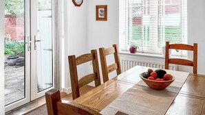 A dining area with a table, chairs, a bowl of fruit, a clock, and a window with blinds.