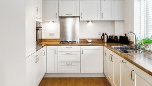 A modern kitchen with white cabinets, a stainless steel range hood, wooden countertops, and a built-in sink.