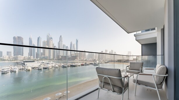 Un balcone con vista sullo skyline cittadino, una ringhiera in vetro e due sedie.