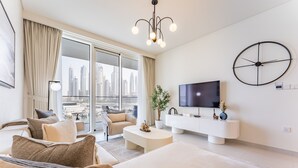 Un soggiorno moderno con una grande TV, un orologio a parete rotondo e vista sulla città attraverso ampie finestre a tutta altezza.