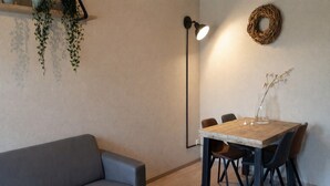 Ein modernes Wohnzimmer mit einer grauen Couch, einem Holzesstisch mit Stühlen, einer Stehlampe und einer hängenden Pflanze.