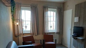 Ein Wohnzimmer mit einer Couch, zwei Sesseln, einem Couchtisch, einem an der Wand montierten Fernseher und einer Heizung.