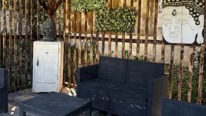 Un área de estar al aire libre con mobiliario de mimbre, un refrigerador blanco y decoración en la pared.