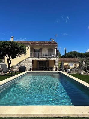Une maison à deux étages avec une piscine, des marches en pierre et du mobilier d’extérieur.