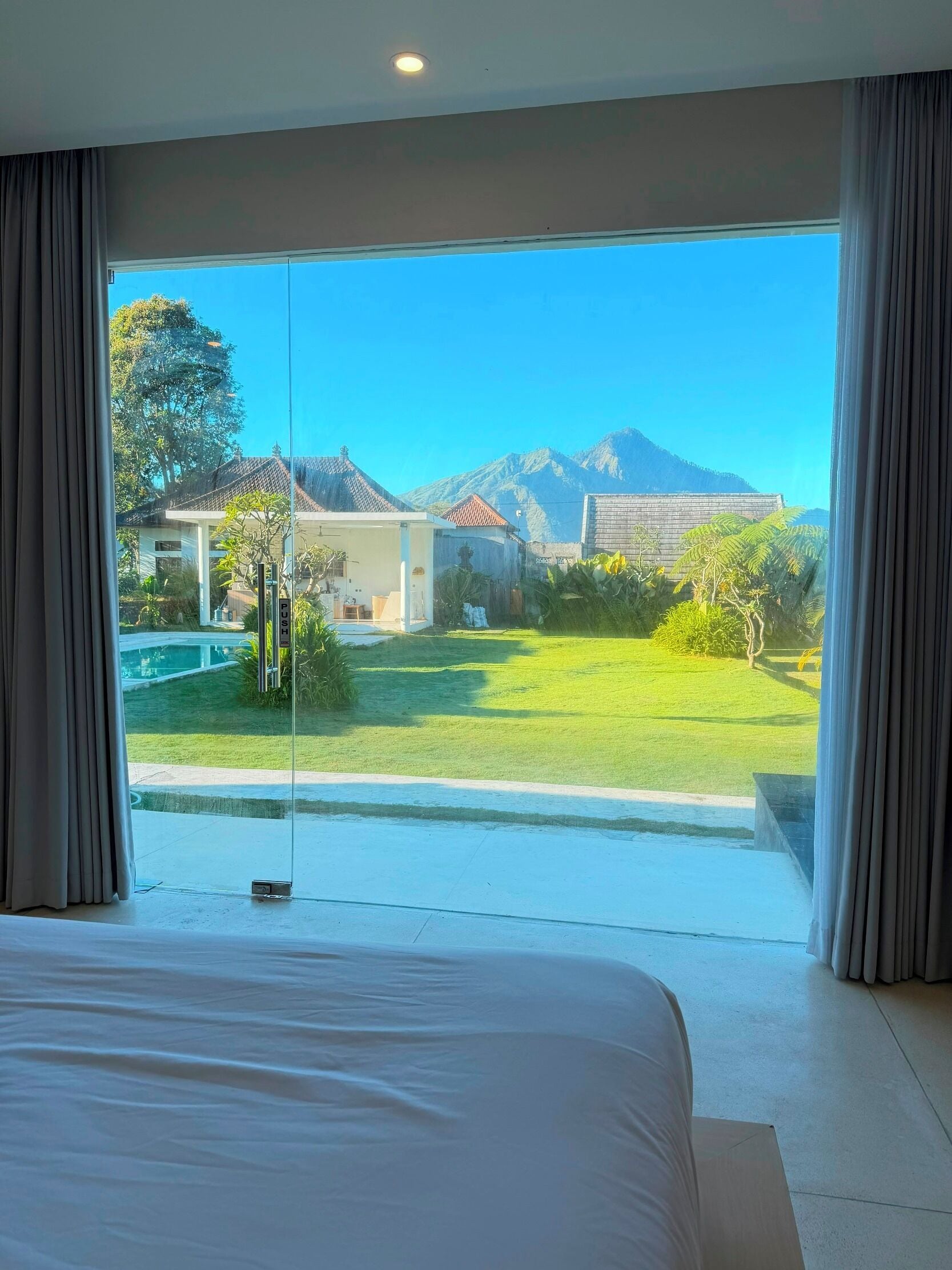 A bedroom with a large bed, a view of a house, and a mountain in the background.