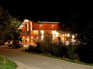 Ein mehrstöckiges Holzhaus mit Balkon, einer Veranda und einer Auffahrt mit geparkten Autos.