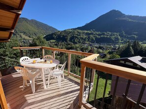 Een houten terras met een tafel en stoelen, met uitzicht op een bergachtig landschap.