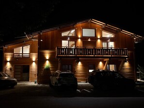 A two-story wooden cabin with a balcony, multiple windows, and a carport with two cars parked. - Spacious and bright, in a chalet, with superb mountain views, near Morzine (Saint-Jean-d'Aulps)
