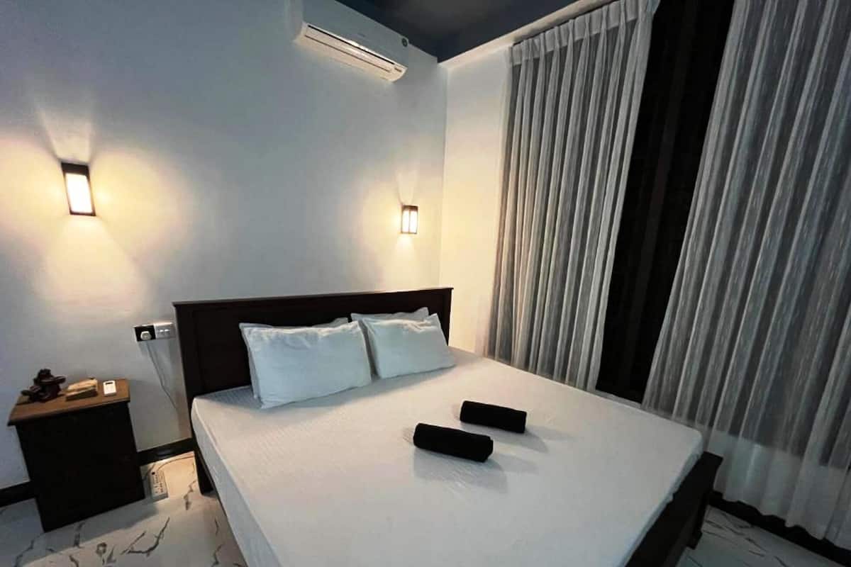 Una habitación de hotel con una cama grande, dos mesitas de noche, aire acondicionado de pared y una ventana con cortinas.
