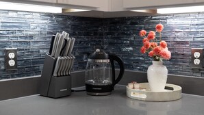 Una cucina moderna con uno schienale piastrellato nero e grigio, una macchina per il caffè, un portacoltelli e un vaso con fiori sul bancone.