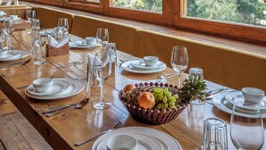 A wooden dining table set with white plates, glasses, and a fruit basket. - ELIVAAS Everly Luxury 1BHK Entire Home (Kumharsain)