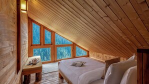 Quarto de cabana de madeira com teto inclinado, um banco de madeira com mesa e uma cama com almofadas.