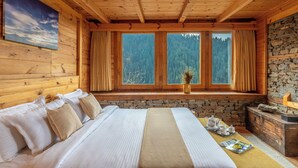 A wooden cabin room with a bed, a stone fireplace, and a window with curtains. - ELIVAAS Everly Luxury 1BHK Entire Home (Kumharsain)