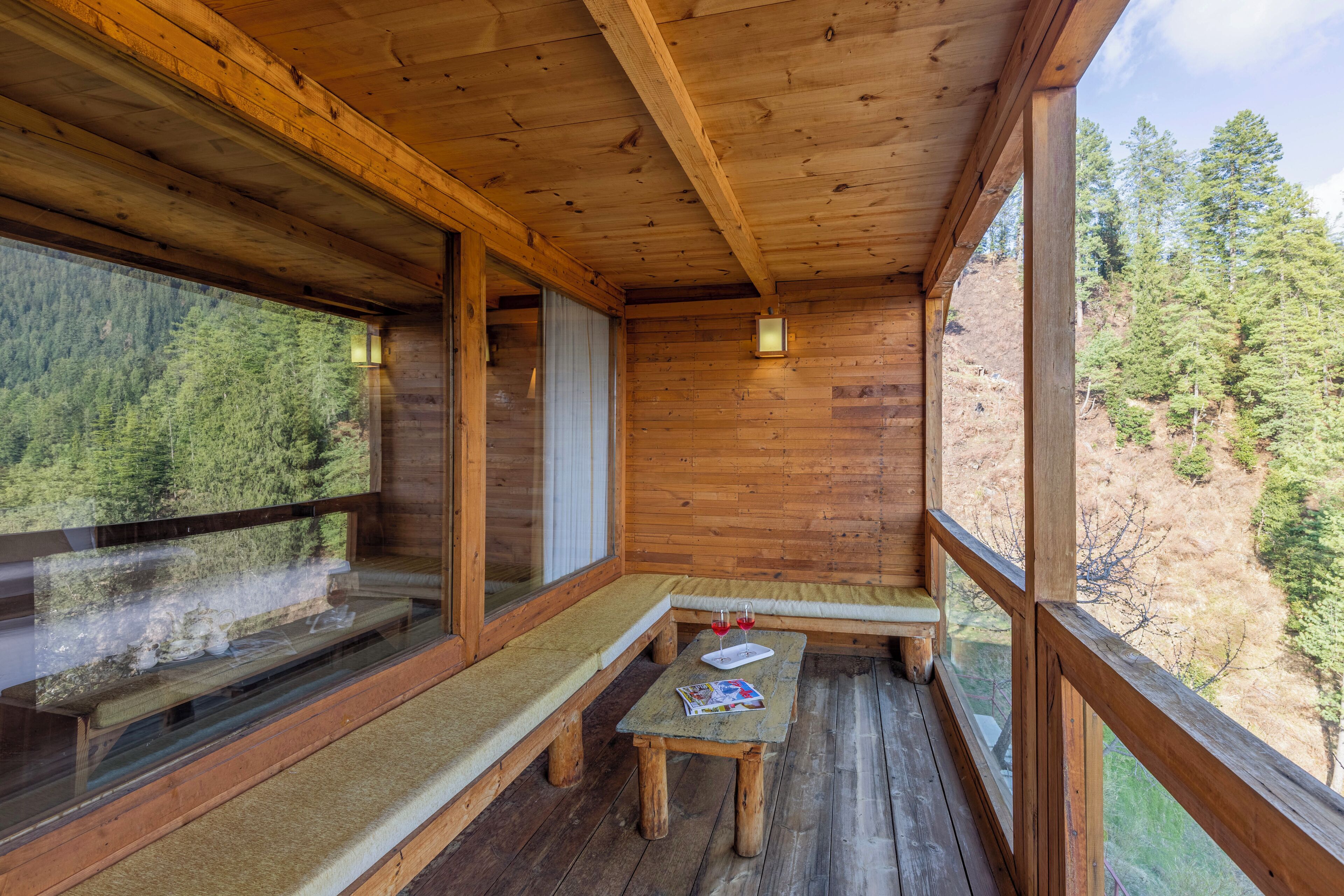 A wooden cabin with a wooden deck, a bench, and a table with a tray and glasses.