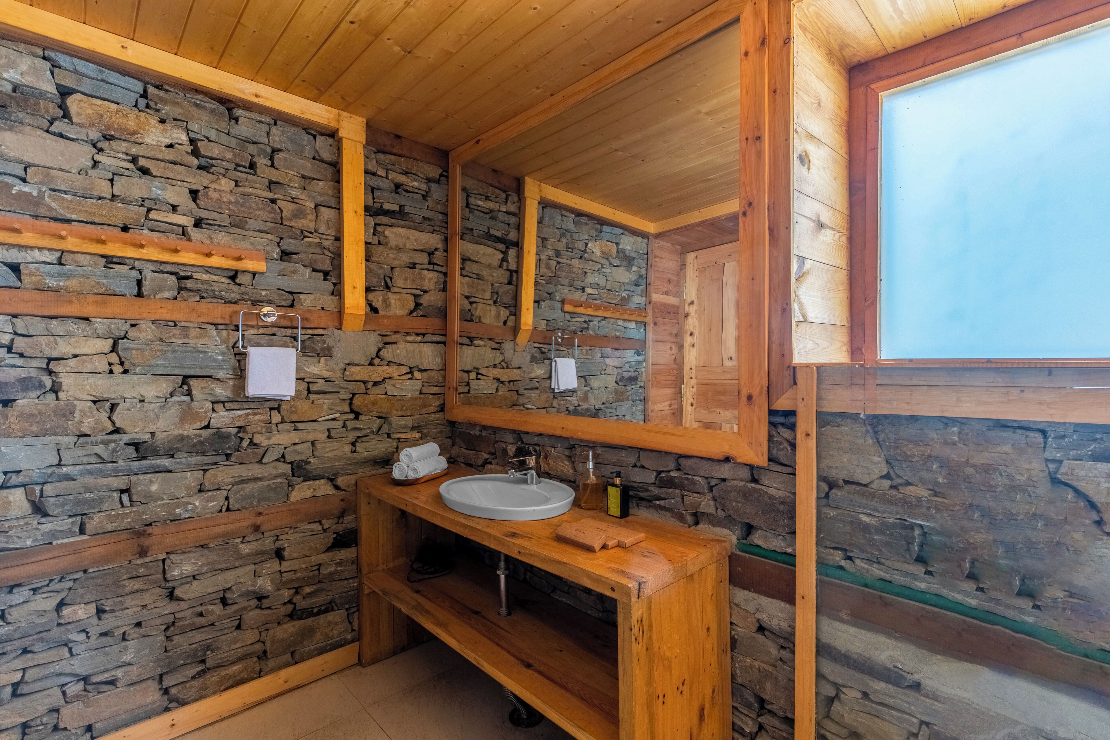 A bathroom with a stone wall, wooden beams, a large mirror, a sink, and a wooden vanity.