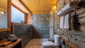 A bathroom with stone walls, wooden ceiling, a toilet, a sink, and a towel rack. - ELIVAAS Everly Luxury 1BHK Entire Home (Kumharsain)