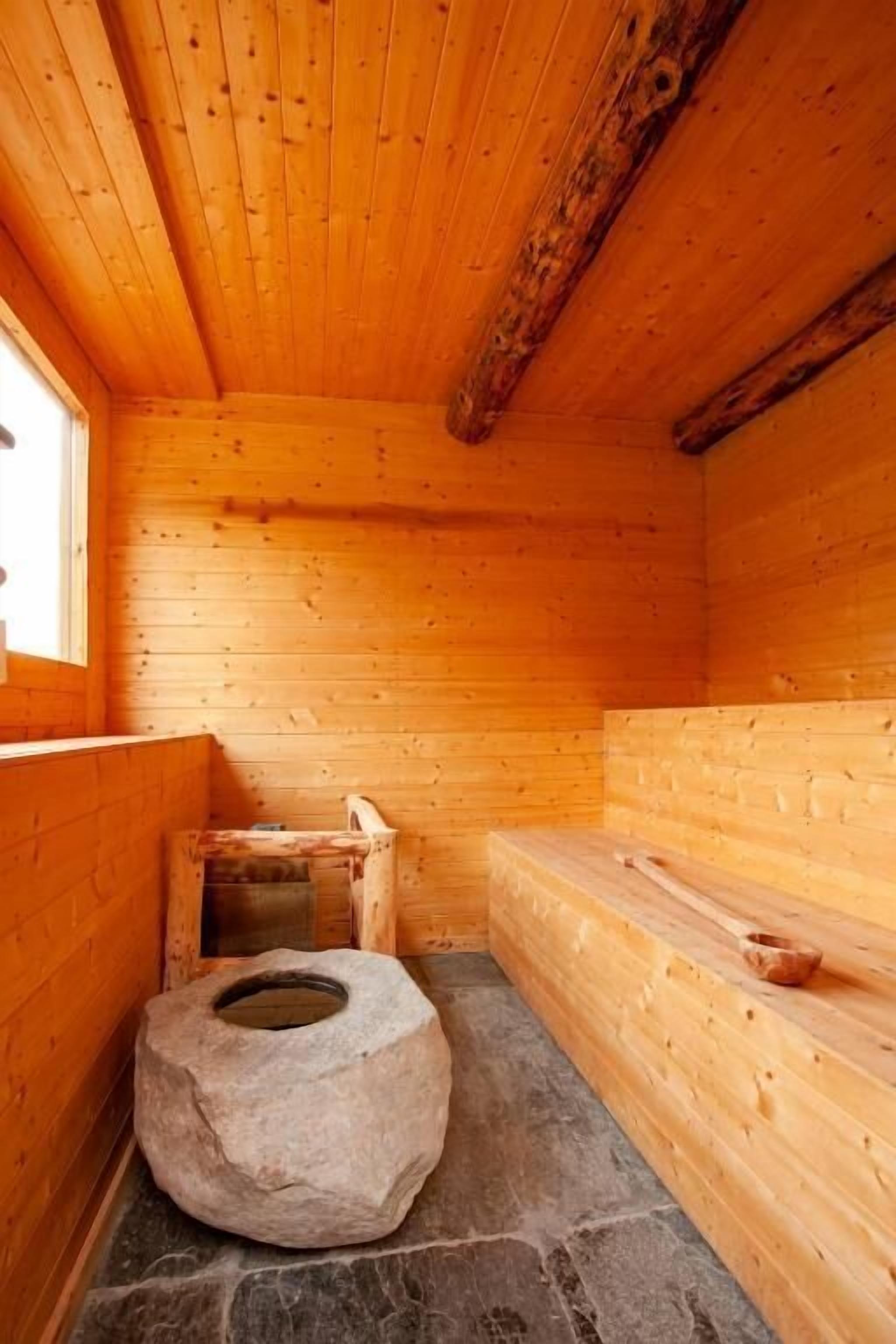 Un sauna en bois avec un banc en pierre, un siège en pierre et un sol en pierre.