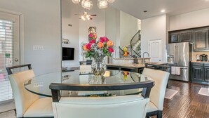 Eine moderne Küche mit einem Glastisch, weißen Stühlen, einem Edelstahlkühlschrank und einer dekorativen Vase mit Blumen.