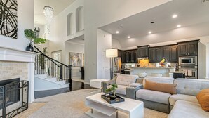 Ein modernes Wohnzimmer mit Kamin, einer Treppe und einem Küchenbereich mit dunklen Schränken und Edelstahlgeräten.